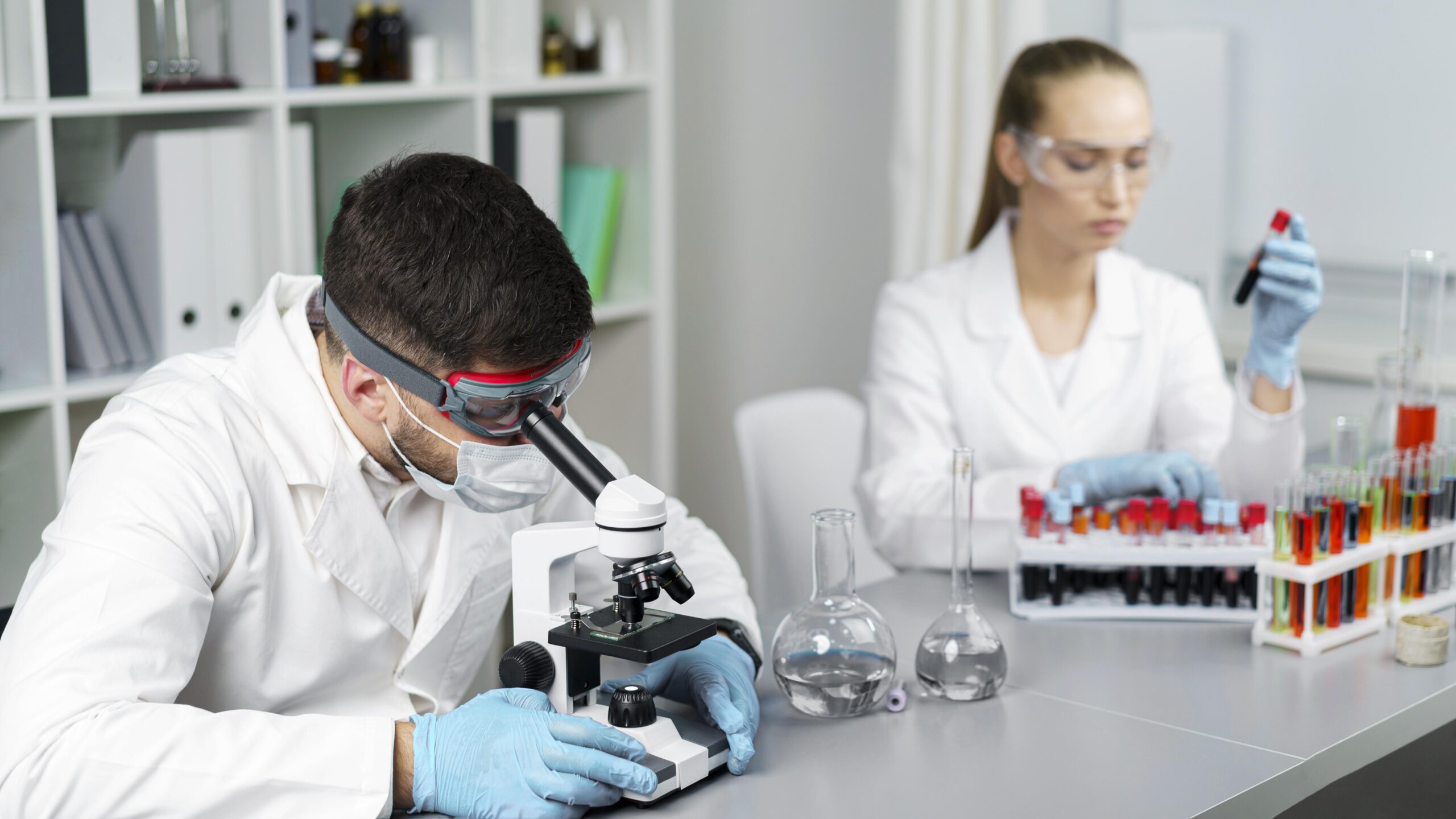 female researcher male colleague laboratory with test tubes safety glasses